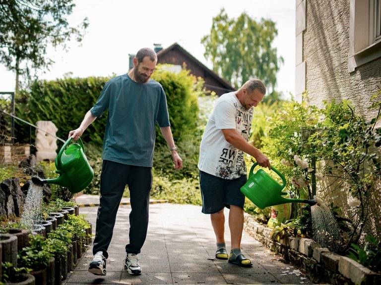 Zwei Männer gießen Blumen.