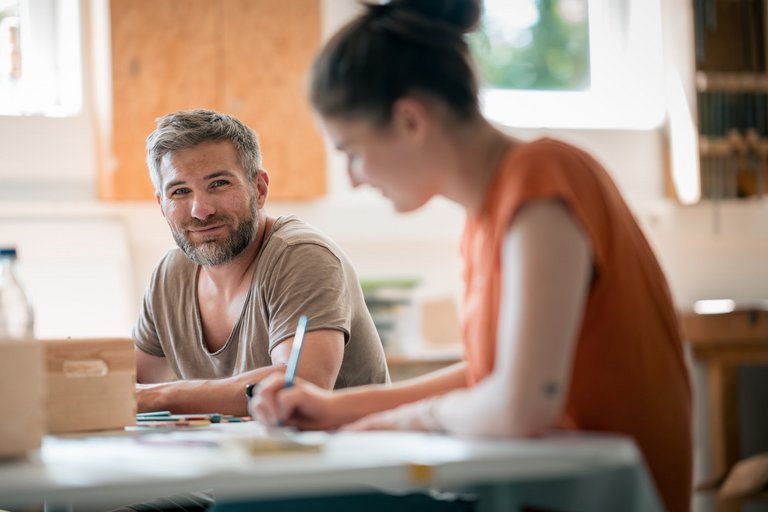 Eine junge Frau und ein Mann sitzen an einem Tisch und zeichnen.